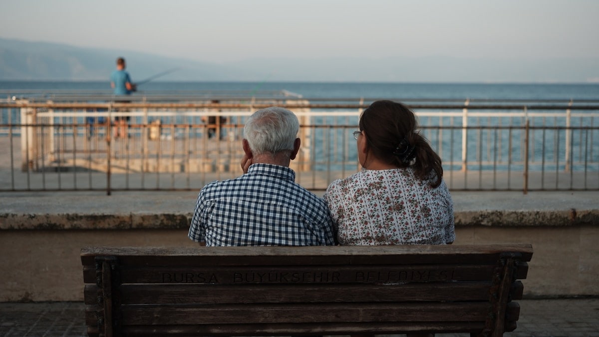 a man and a woman sitting on a bench looking at the ocean